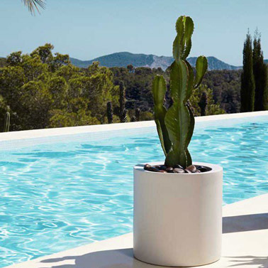 ¡Optamos por una maceta cilíndrica para decorar la piscina con clase!  De color blanco, alberga un cactus y guijarros para un efecto decorativo superior. 