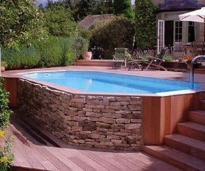 Dispuesta debajo de la terraza de madera, esta encantadora piscina sobre el suelo con piedra y madera en un estilo auténtico realzará su decoración al aire libre.