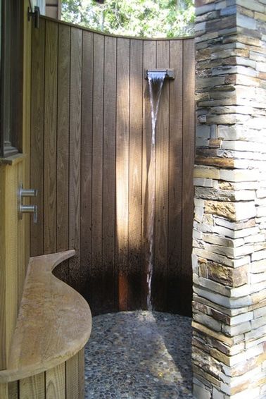 Una ducha de jardín instalada en un patio construido en redondeado con tablones de teca y un pilar de piedra para completar el redondeo.