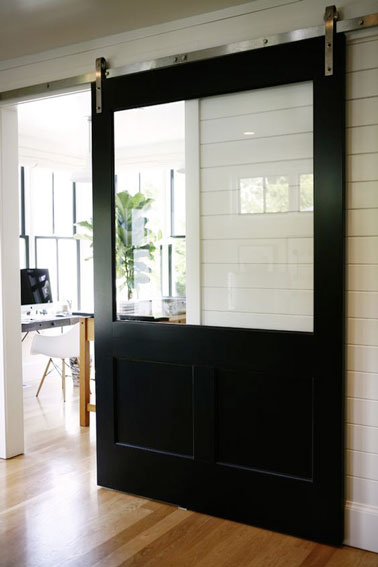 Esta puerta corredera de madera pintada en negro y decorada con un gran ventanal que deja pasar la luz, embellece la decoración de la casa de este arquitecto. 