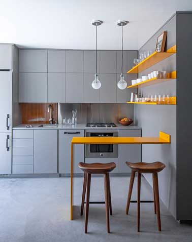 Con el gris, la pequeña cocina adquiere profundidad.  El color naranja brillante de los estantes y la esquina de la mesa le da ritmo a la decoración y le da tono a la habitación