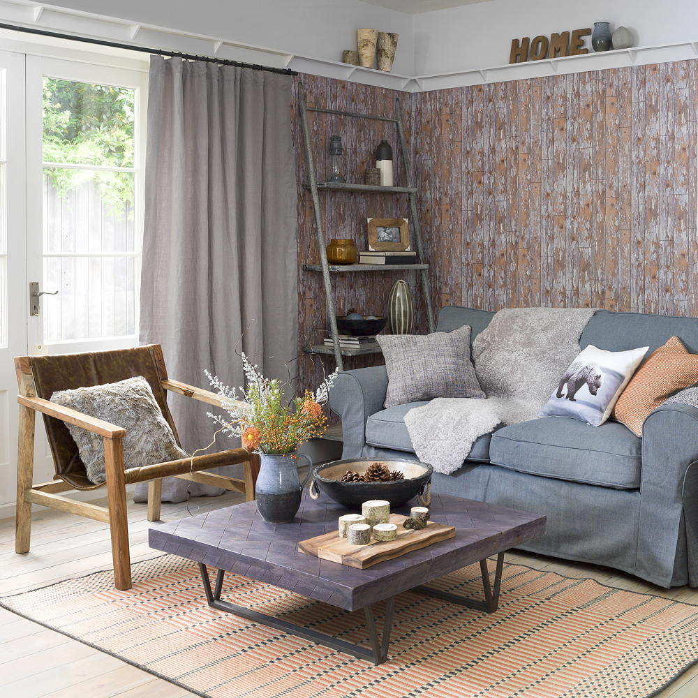 Sala de estar rústica con papel tapiz de efecto madera en gris y naranja quemado con sofá gris y silla decorativa de madera